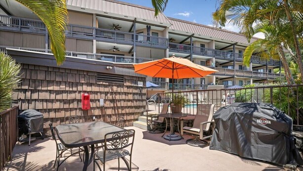 Une terrasse d’hôtel avec des meubles d’extérieur, un barbecue abrité et une piscine en arrière-plan.