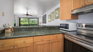 Une cuisine avec des meubles de rangement en bois, un four à micro-ondes, un four traditionnel et un ventilateur de plafond.