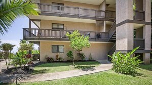 Un immeuble à plusieurs étages doté de balcons, d’une pelouse bien entretenue et de diverses plantes.