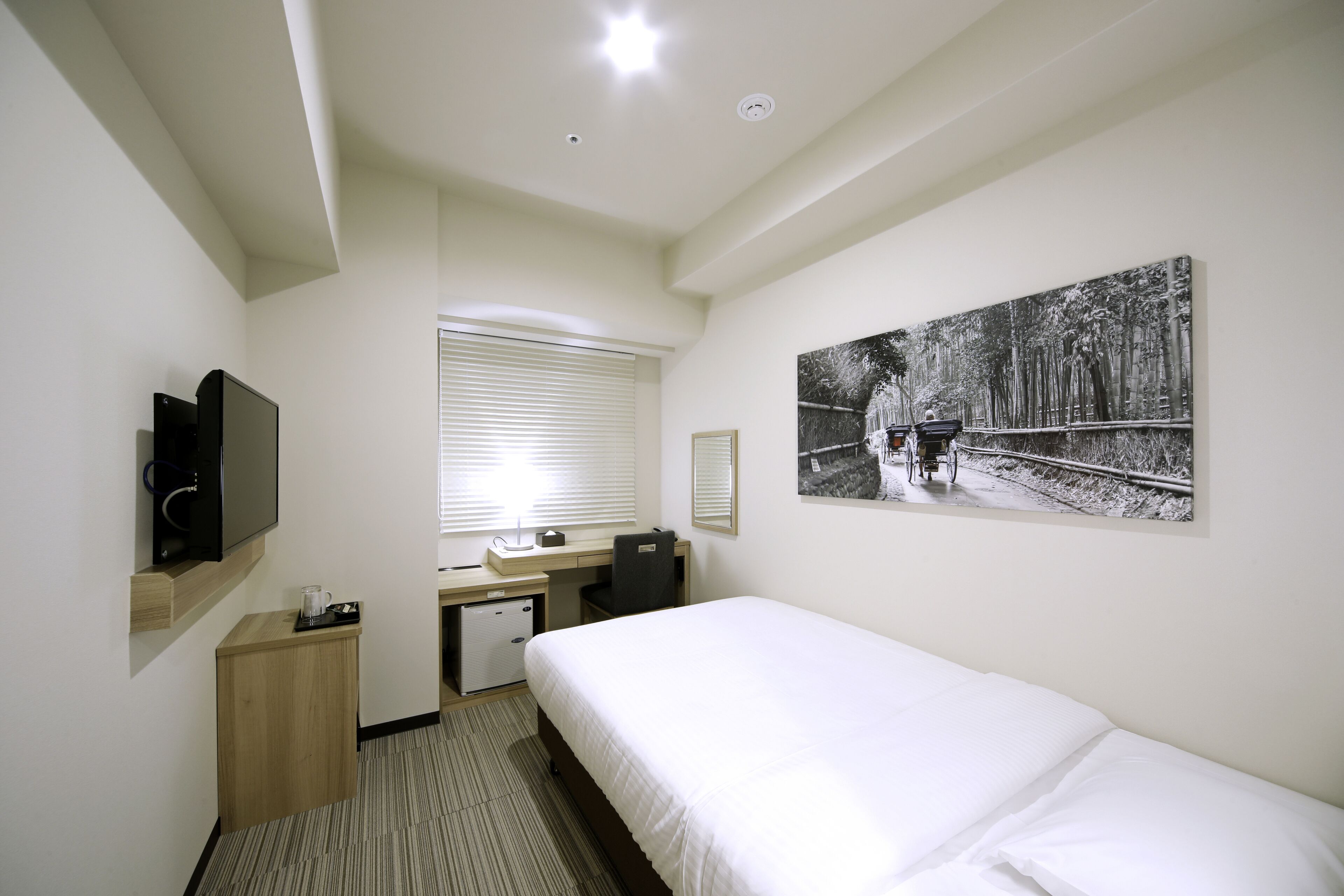 A hotel room with a bed, desk, chair, TV, and a painting on the wall.