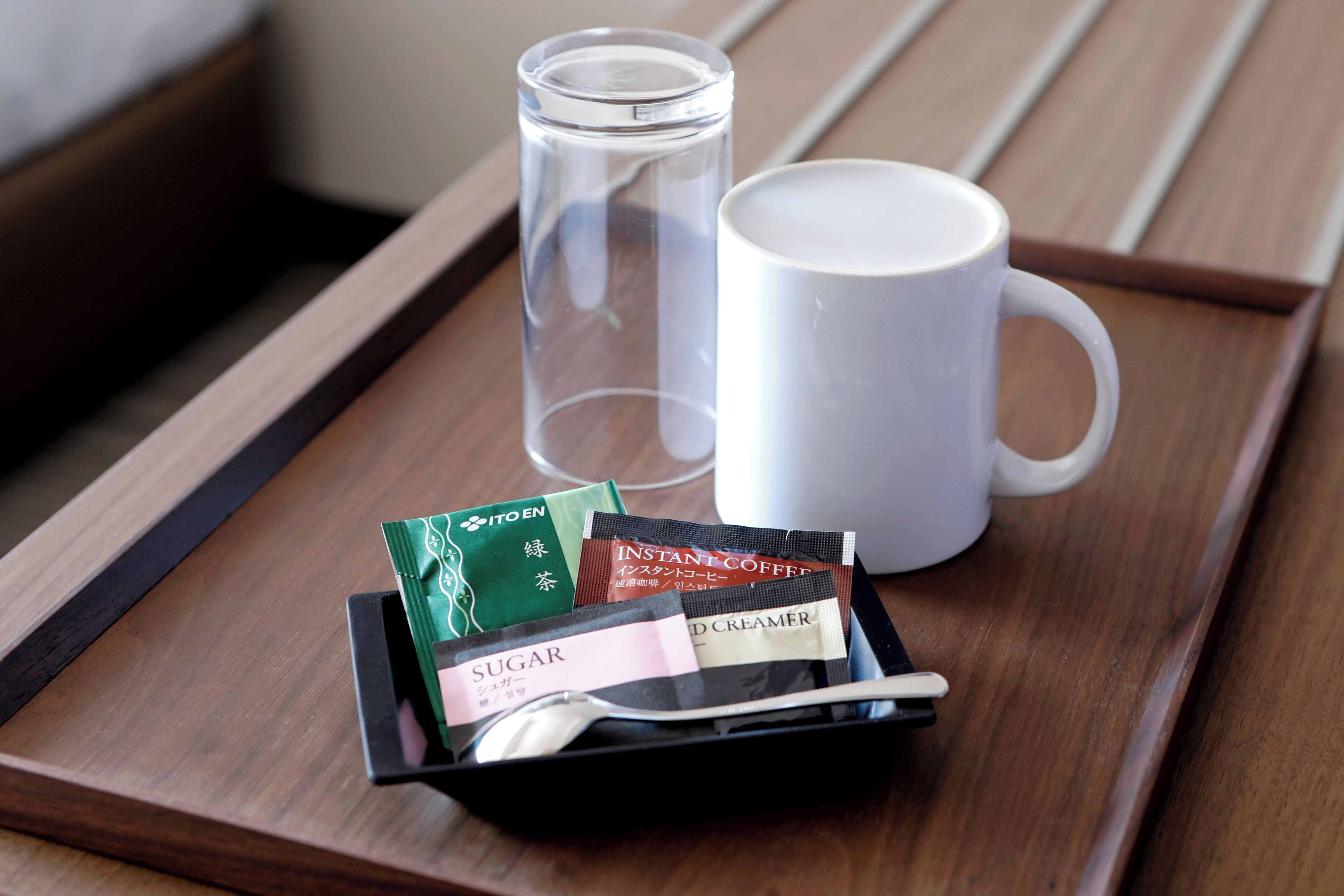 A tray with a white mug, a glass, and sachets of instant coffee, sugar, and cream on a wooden surface.