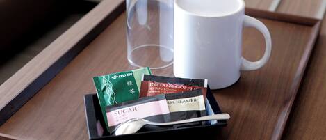 A tray with a white mug, a glass, and sachets of instant coffee, sugar, and cream on a wooden surface.