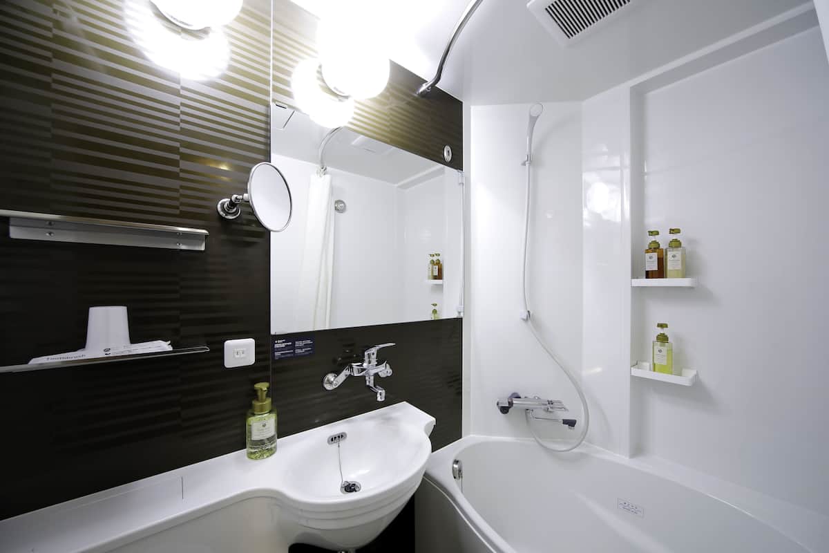 A modern bathroom with a white sink, a mirror, a shower, and two shelves with toiletries.