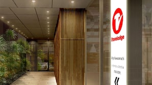 A hallway with a vertical bamboo screen, a Travelodge sign, and a small indoor garden with various plants.