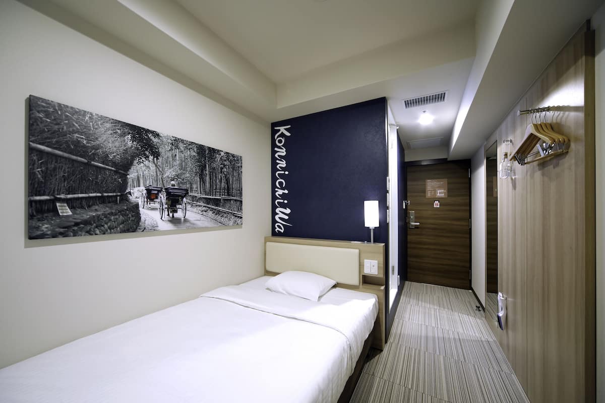 A hotel room with a bed, a large black and white photograph on the wall, a wooden wardrobe, and a mirror.