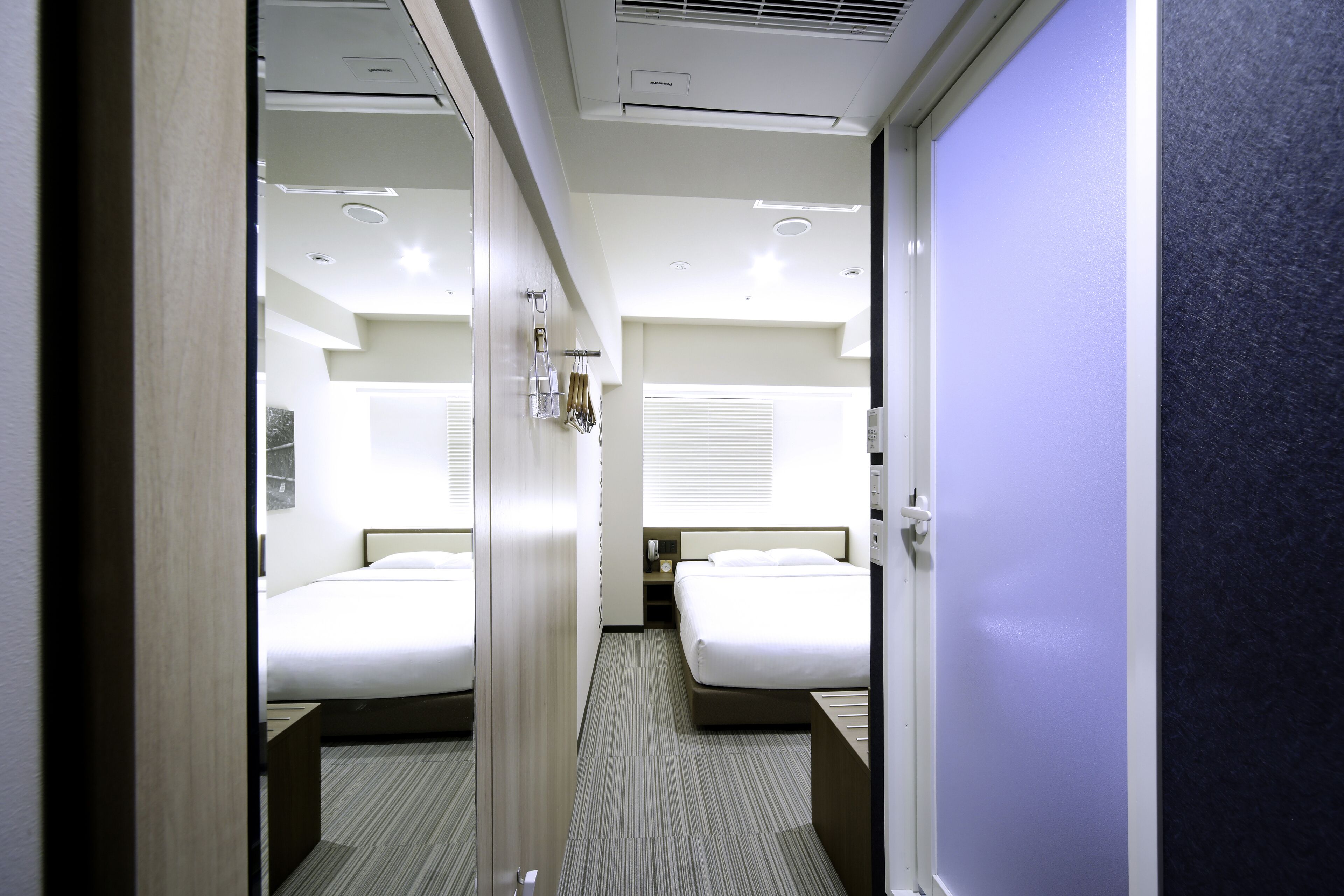 Une chambre d’hôtel avec deux lits, une table de chevet, une commode et une fenêtre avec des stores.