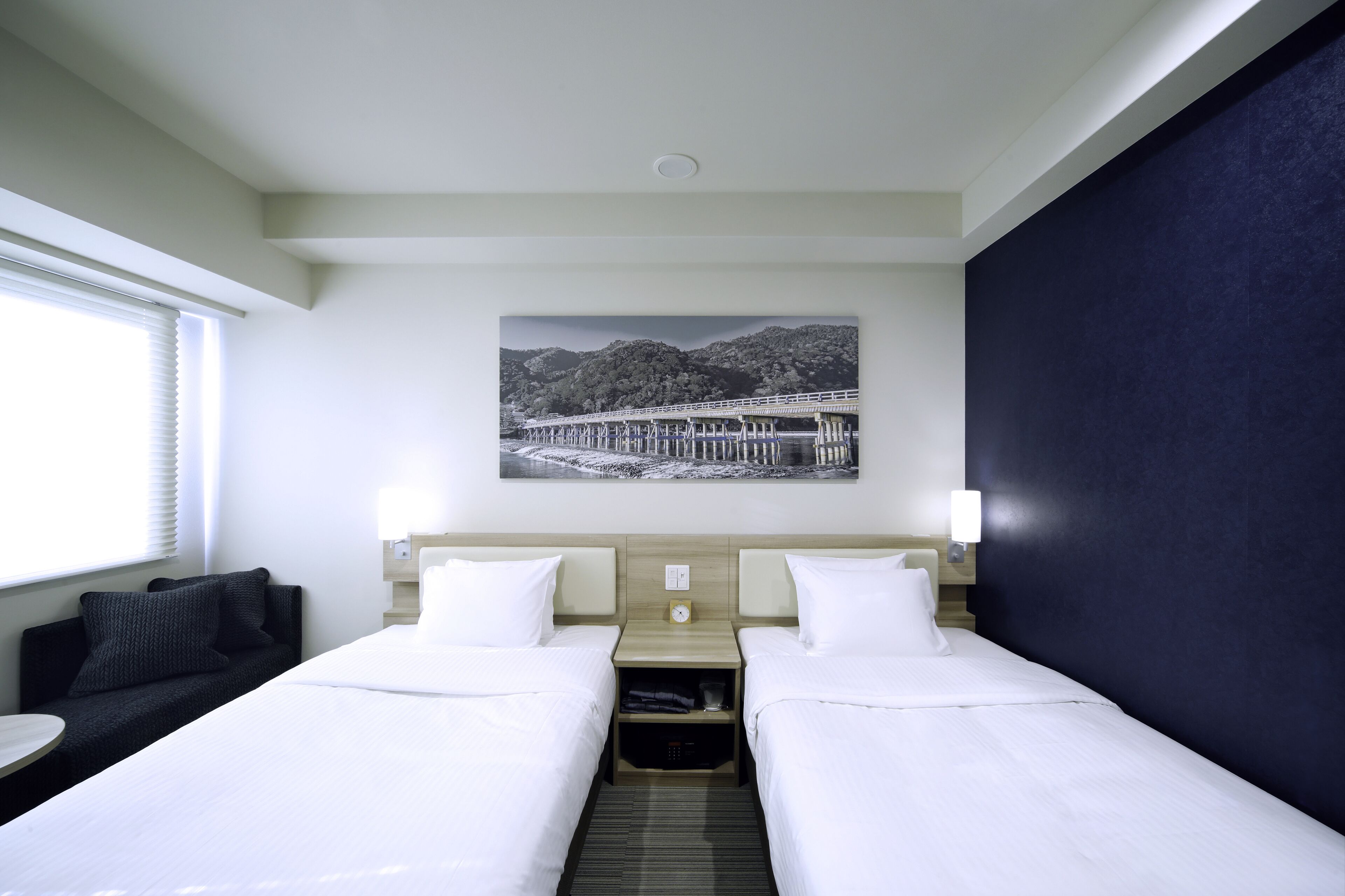 A hotel room with two beds, a sofa, a small table, and a wall-mounted picture.