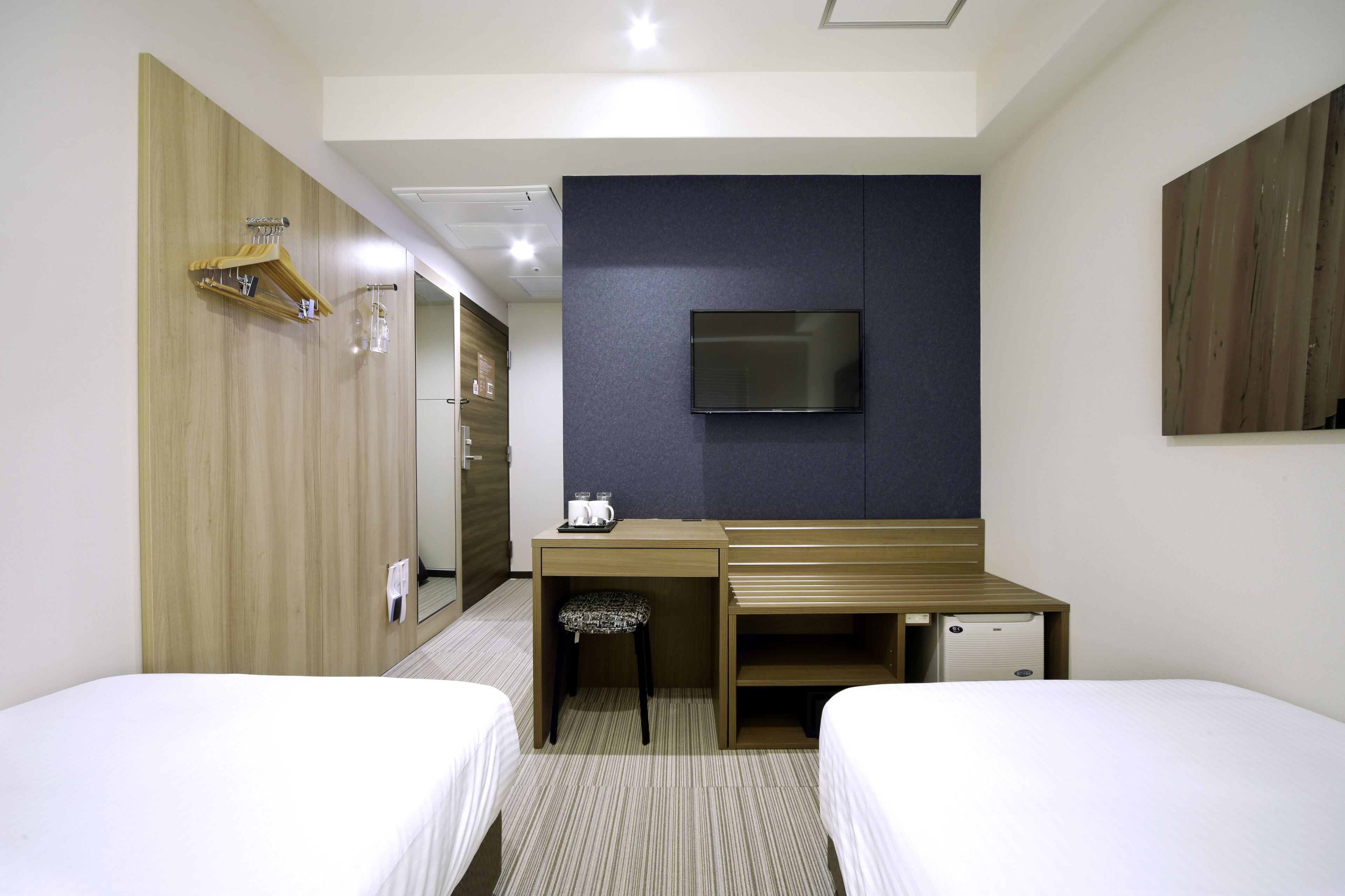 A hotel room with two beds, a desk with a chair, a television, and a wardrobe.