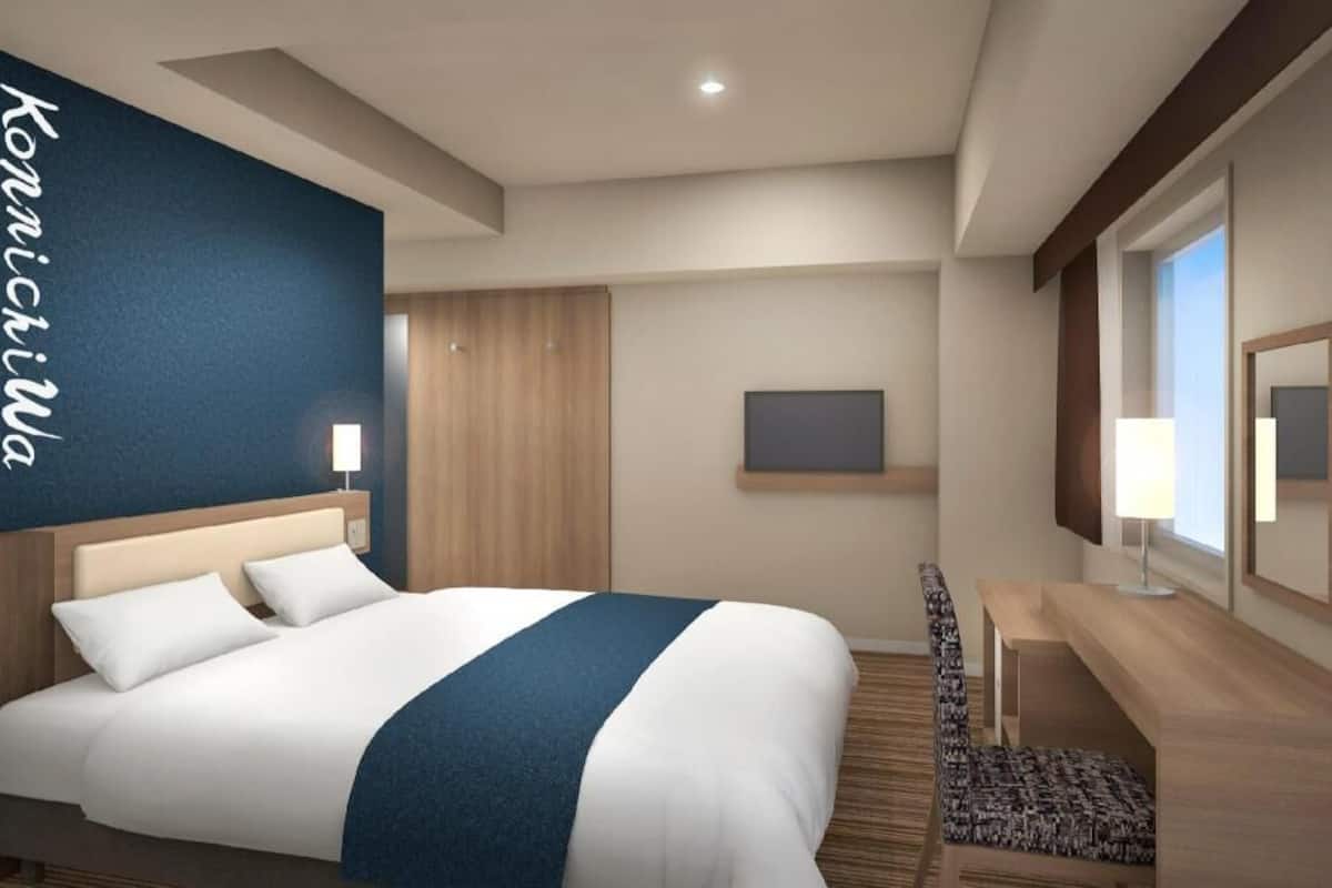 A hotel room with a large bed, a desk, a chair, a TV, and a window.