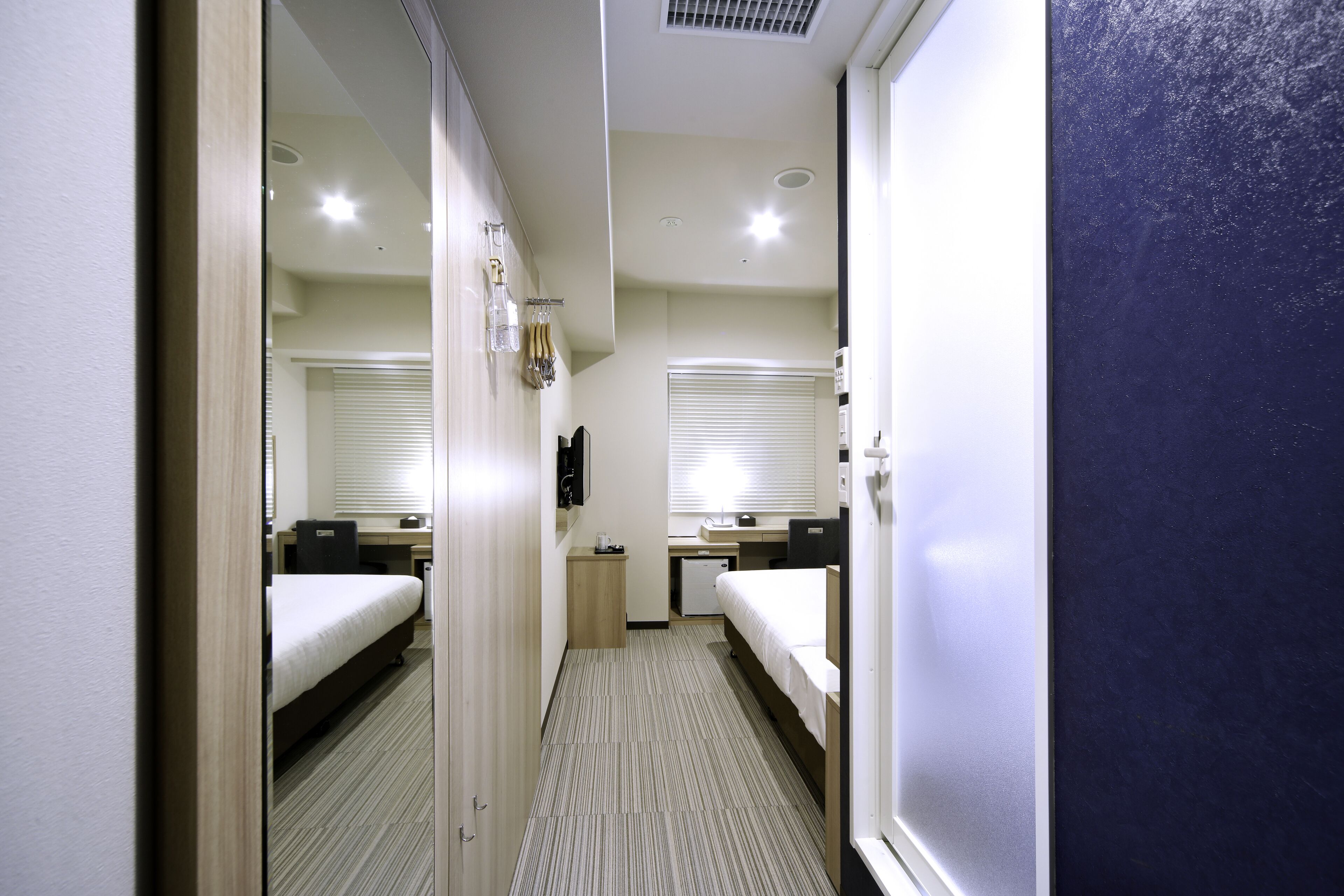 A hotel room with two beds, a desk, a small cabinet, and a mirror.