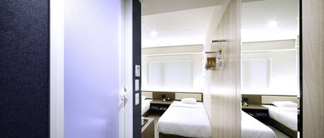 A hotel room with two beds, a desk, a mirror, and a window with blinds.