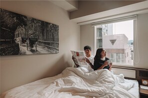 Relax in this serene bedroom with a large bed, a beautiful forest scene painting, and a city view.