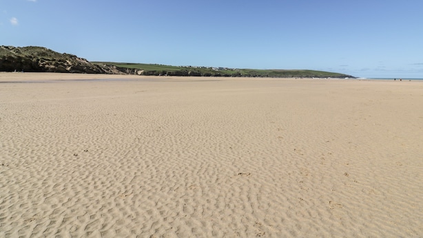 A wide sandy beach with gentle hills in the background and a clear blue sky. - Great Meadow Barn (Newquay)