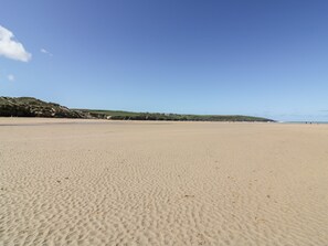 A wide sandy beach with gentle hills in the background and a clear blue sky. - Great Meadow Barn (Newquay)