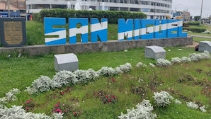 Ein großes, blau-weißes Schild mit der Aufschrift "SAN MIGUEL" vor einem Gebäude mit kreisförmigem Design und einer Fontäne.