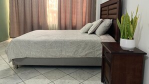 Ein Schlafzimmer mit einem Bett, Vorhängen, einem Nachttisch und einer Topfpflanze.