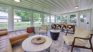 A spacious room with a large window, a round table, a leather sofa, and a dining area with chairs. - The Boathouse on Moon Lake (Ashland)