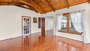 Une pièce spacieuse avec un plancher en bois, un plafond en pente et de grandes fenêtres dotées de rideaux.