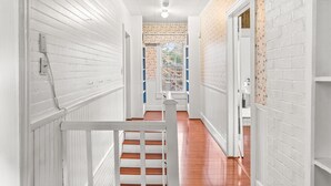 Un couloir aux murs recouverts de panneaux blancs, doté d’un plancher en bois et d’une rambarde blanche.