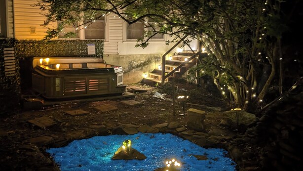 Un jardin avec un jacuzzi, un petit étang et une maison en arrière-plan.