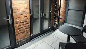 A patio area with a brick wall, two sliding glass doors, a metal table, and two chairs.