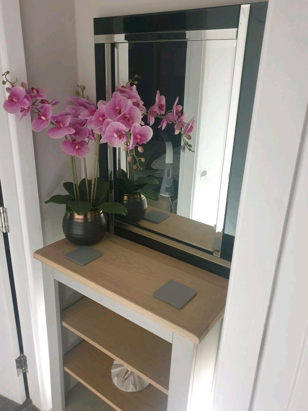 Un tocador de baño con un espejo, dos orquídeas en macetas y una pequeña estantería.