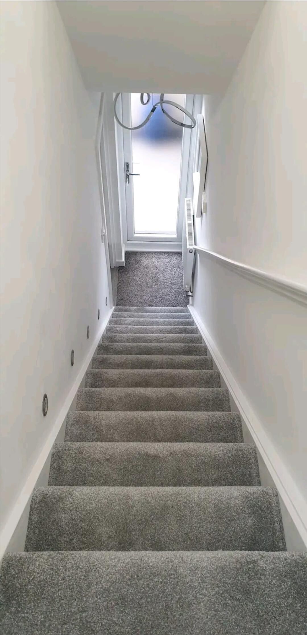 A carpeted staircase with white walls and a door at the top.