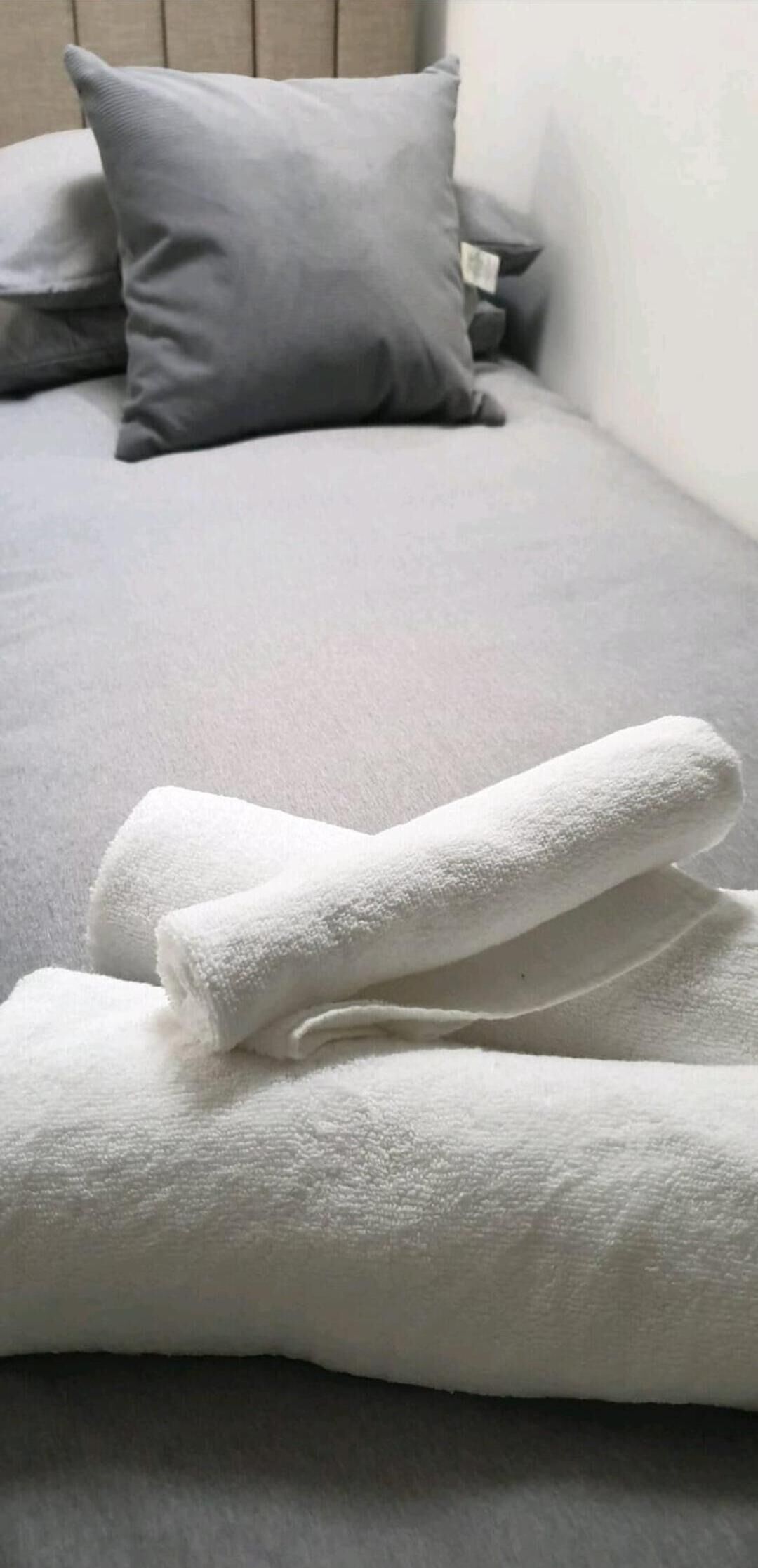Cama com roupa de cama cinza e duas toalhas brancas dispostas sobre ela.