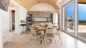 A modern kitchen with an arched ceiling, a dining area with a table set for four, and a view of the sea through large sliding doors. - 2475 Villa Pietra del Sole by Perle di Puglia (Salve)