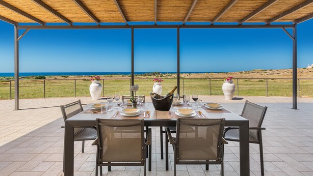 An outdoor dining area with a table set for four, overlooking a coastal landscape. - 2475 Villa Pietra del Sole by Perle di Puglia (Salve)