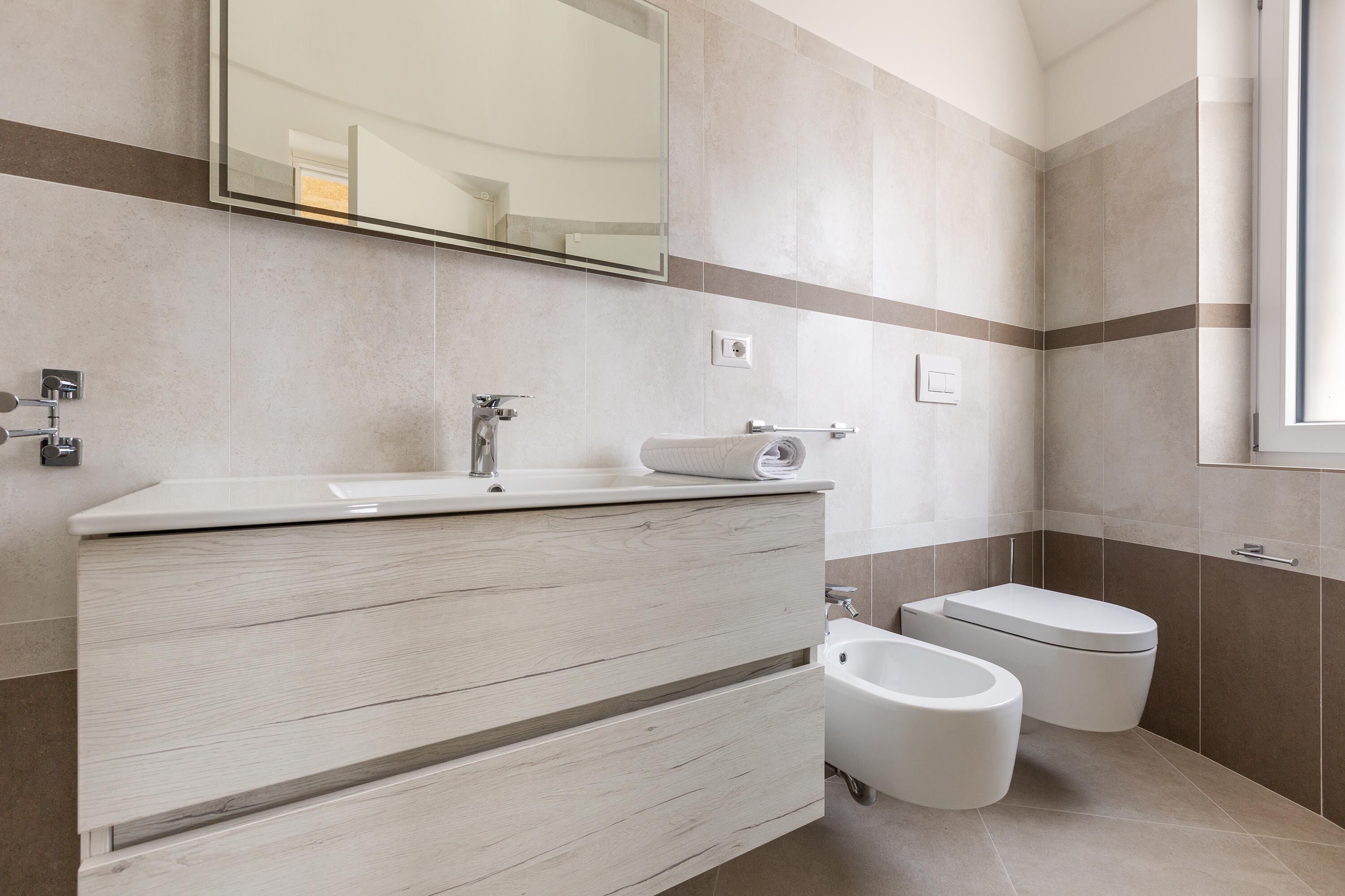 A modern bathroom with a wooden vanity, a toilet, and a bidet.