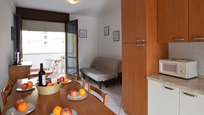 Une cuisine compacte avec des meubles en bois, un four à micro-ondes et une table à manger agrémentée de fruits et d’une bouteille.