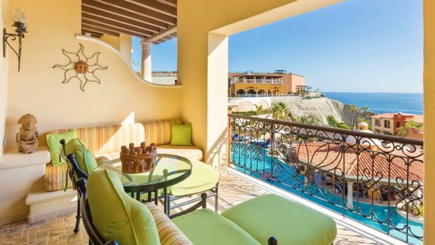 Un balcone con vista su una piscina e l'oceano, con un tavolo e sedie, e un decoro a forma di sole sulla parete.