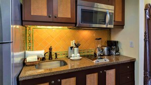 Una cucina con mobili marroni, un frigorifero in acciaio inossidabile, un forno a microonde, un lavello con cestello e una macchina da caffè.