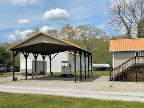 A covered outdoor area with a gravel floor, a building with a metal roof, and a staircase leading to a second-floor level. - 2 RV spots  full hookup, 30&50 amp sewer & water . In City limits of Sunbright (Sunbright)