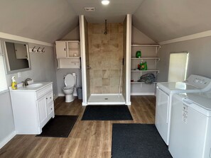 A compact bathroom with a shower, toilet, sink, and a washing machine.