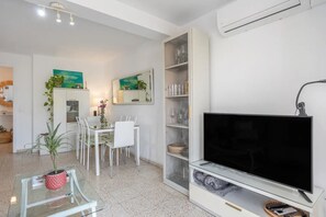 Ein modernes Wohnzimmer mit Flachbildfernseher, Essbereich mit Stühlen, einem Glastisch und einem Blumentopf.