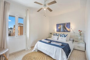 Ein Schlafzimmer mit Bett, Deckenventilator, einem Fenster mit Vorhängen und einem Bild an der Wand.