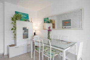 Un comedor moderno con una mesa de vidrio, sillas blancas, un armario blanco y un espejo en la pared.