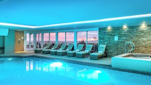 Una piscina interior moderna con sillones de descanso y un muro de piedra.