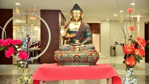 A Buddha statue on a red table with decorative vases of flowers. - Hotel Platinum Shravasti (Ikauna)