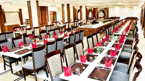 A large banquet hall with long tables set for dining, featuring patterned chairs and red napkins. - Hotel Platinum Shravasti (Ikauna)