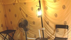 A tent with a patterned yellow interior, a standing fan, a table, and two chairs. - Camp Thar Osian (Jodhpur)