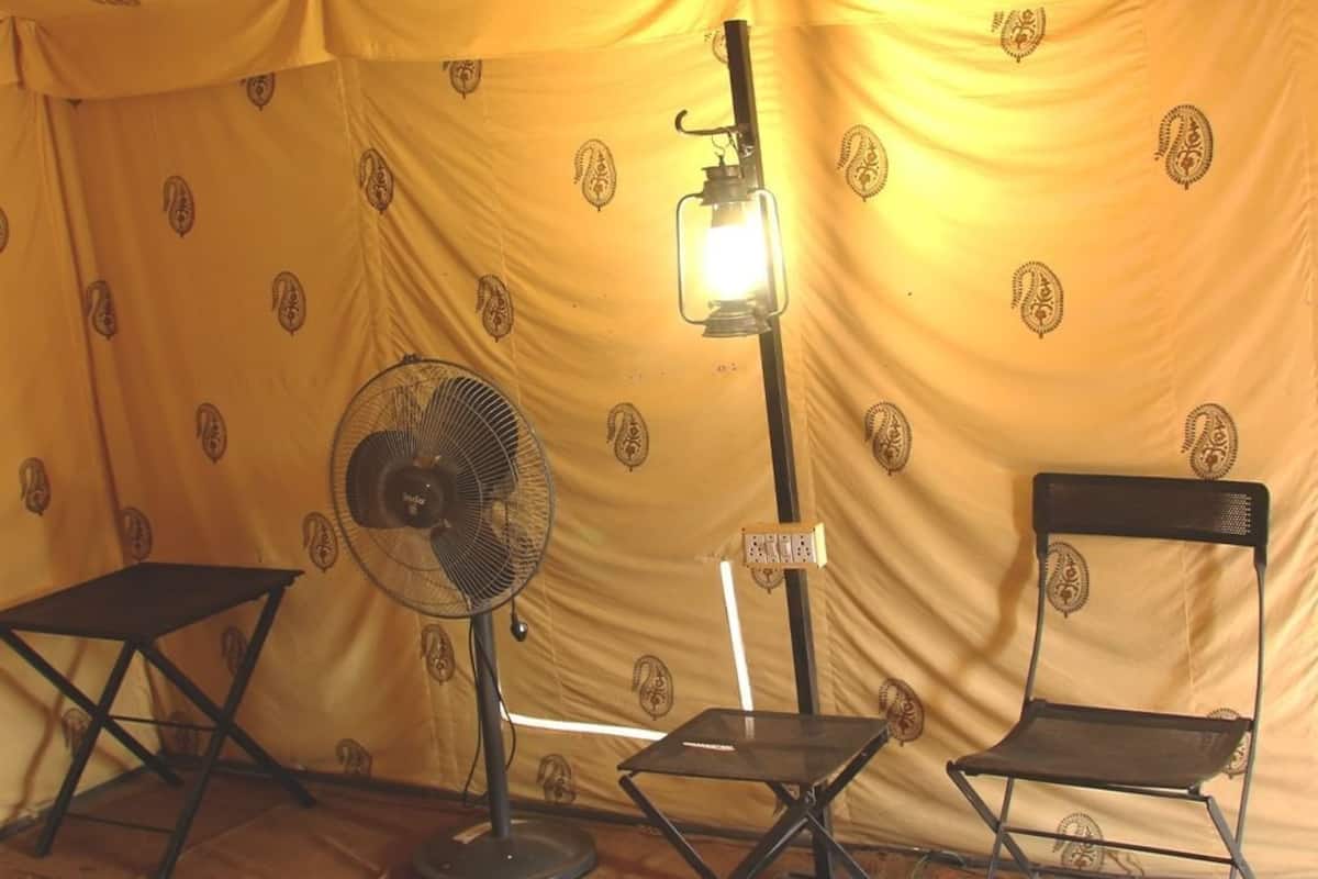 A tent with a patterned yellow interior, a standing fan, a table, and two chairs.