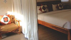 A bedroom with a wooden bed, a chair, and a curtain. - Camp Thar Osian (Jodhpur)