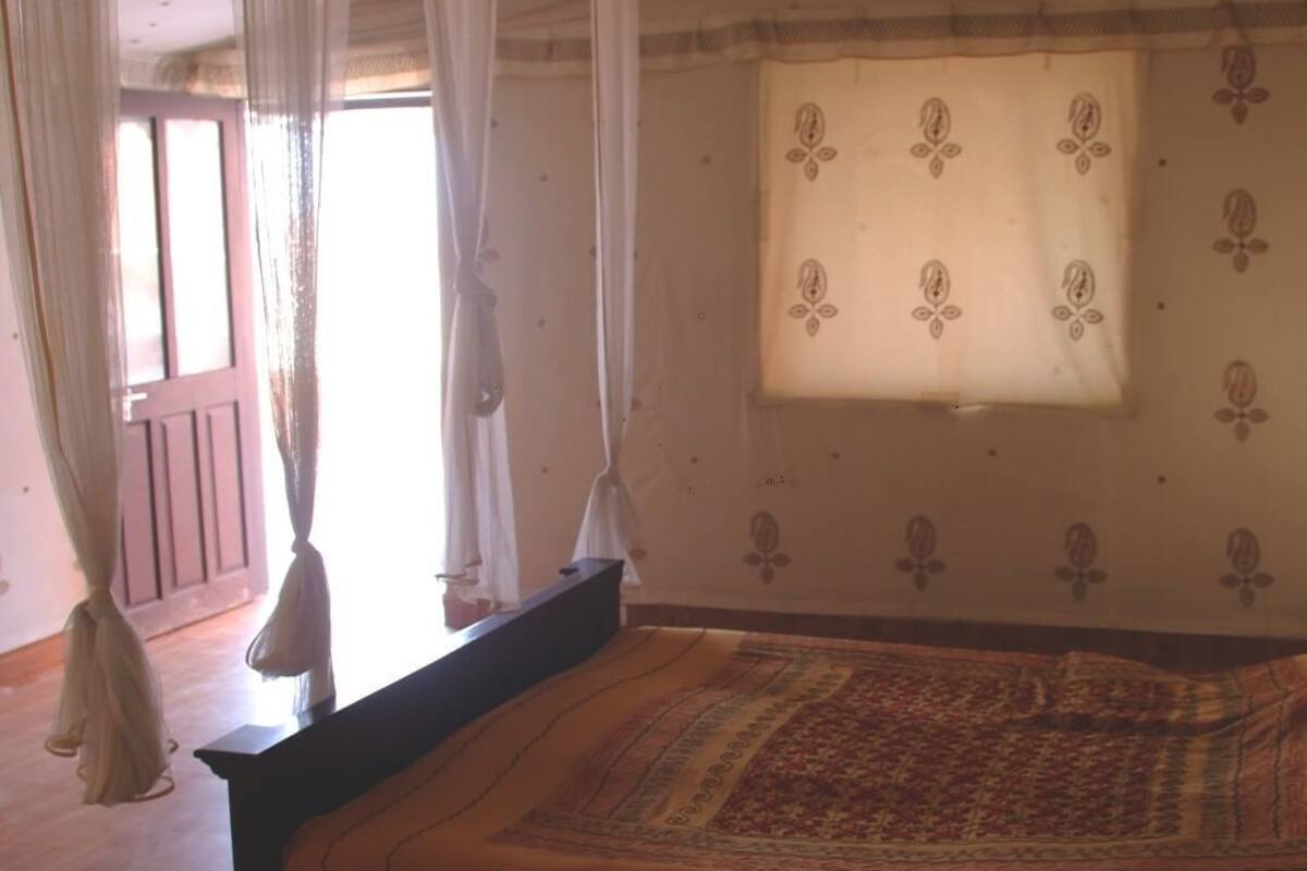 A room with a bed, a window with a patterned curtain, and a view of the outside.