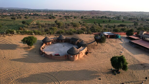 A large, circular building with multiple domed structures, surrounded by a sandy area with sparse vegetation. - Camp Thar Osian (Jodhpur)