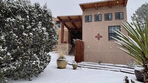 Un edificio de dos pisos con fachada marrón y un emblema rojo. Hay plantas en macetas y una cerca de madera en primer plano.