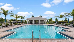 A rectangular swimming pool with a pavilion in the background, surrounded by palm trees and lounge chairs.