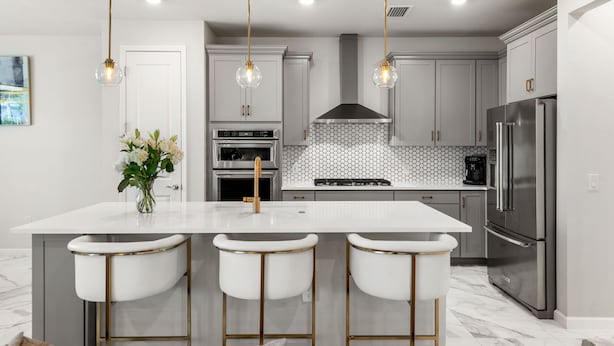 A modern kitchen with a central island, bar stools, stainless steel appliances, and pendant lighting.